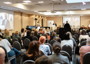 Konferences “Brīvprātīgais darbs Latvijā — vakar, šodien un rīt” foto ar plašu auditoriju, skatuvi un runātāju.
