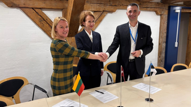 Trīs cilvēki sēž pie galda un paraksta dokumentus; priekšplānā redzami Lietuvas, Latvijas un Igaunijas karodziņi.