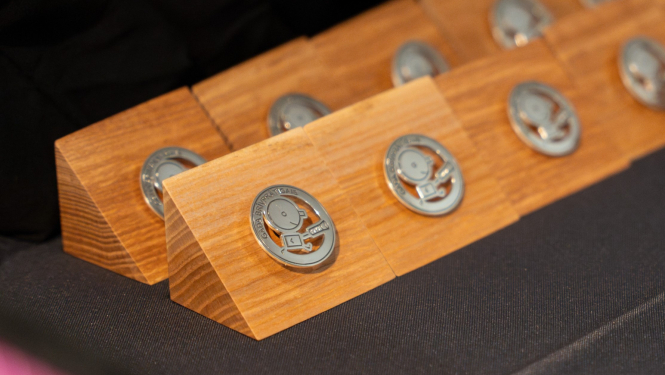 “Gada brīvprātīgais 2025” balvas zīme — metāla emblēma uz koka pamatnes.