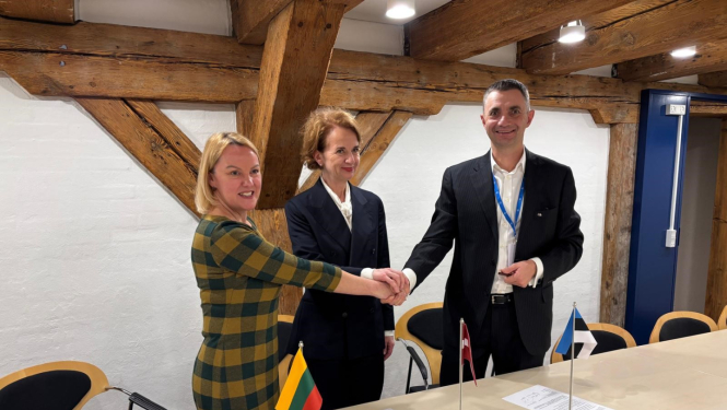 Trīs cilvēki sēž pie galda un paraksta dokumentus; priekšplānā redzami Lietuvas, Latvijas un Igaunijas karodziņi.