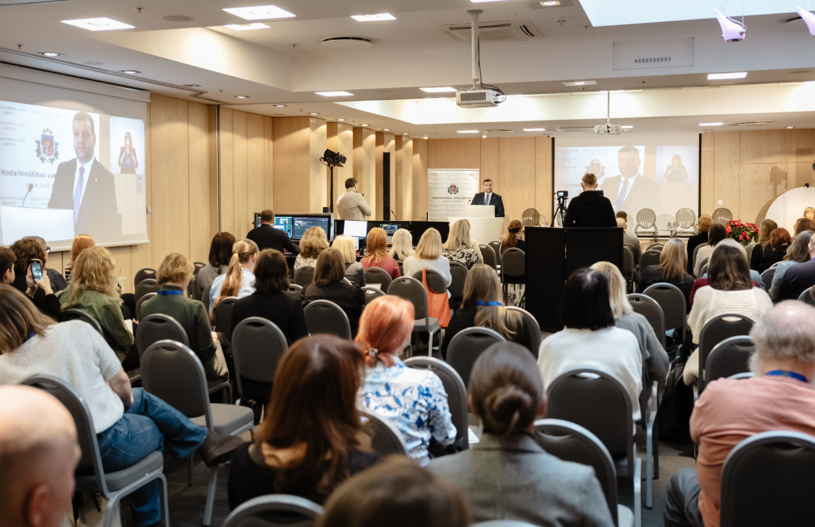 Konferences “Brīvprātīgais darbs Latvijā — vakar, šodien un rīt” foto ar plašu auditoriju, skatuvi un runātāju.
