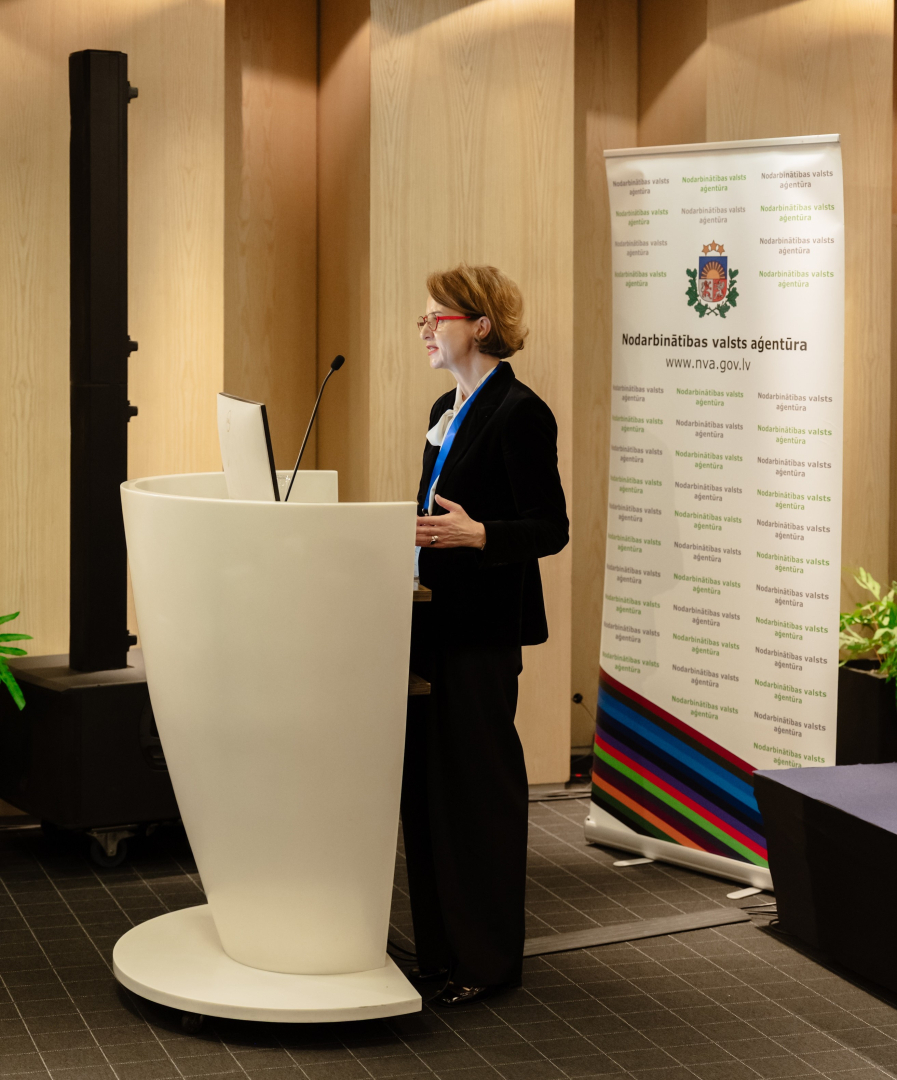 Konferences “Brīvprātīgais darbs Latvijā — vakar, šodien un rīt” foto ar plašu auditoriju, skatuvi un runātāju.
