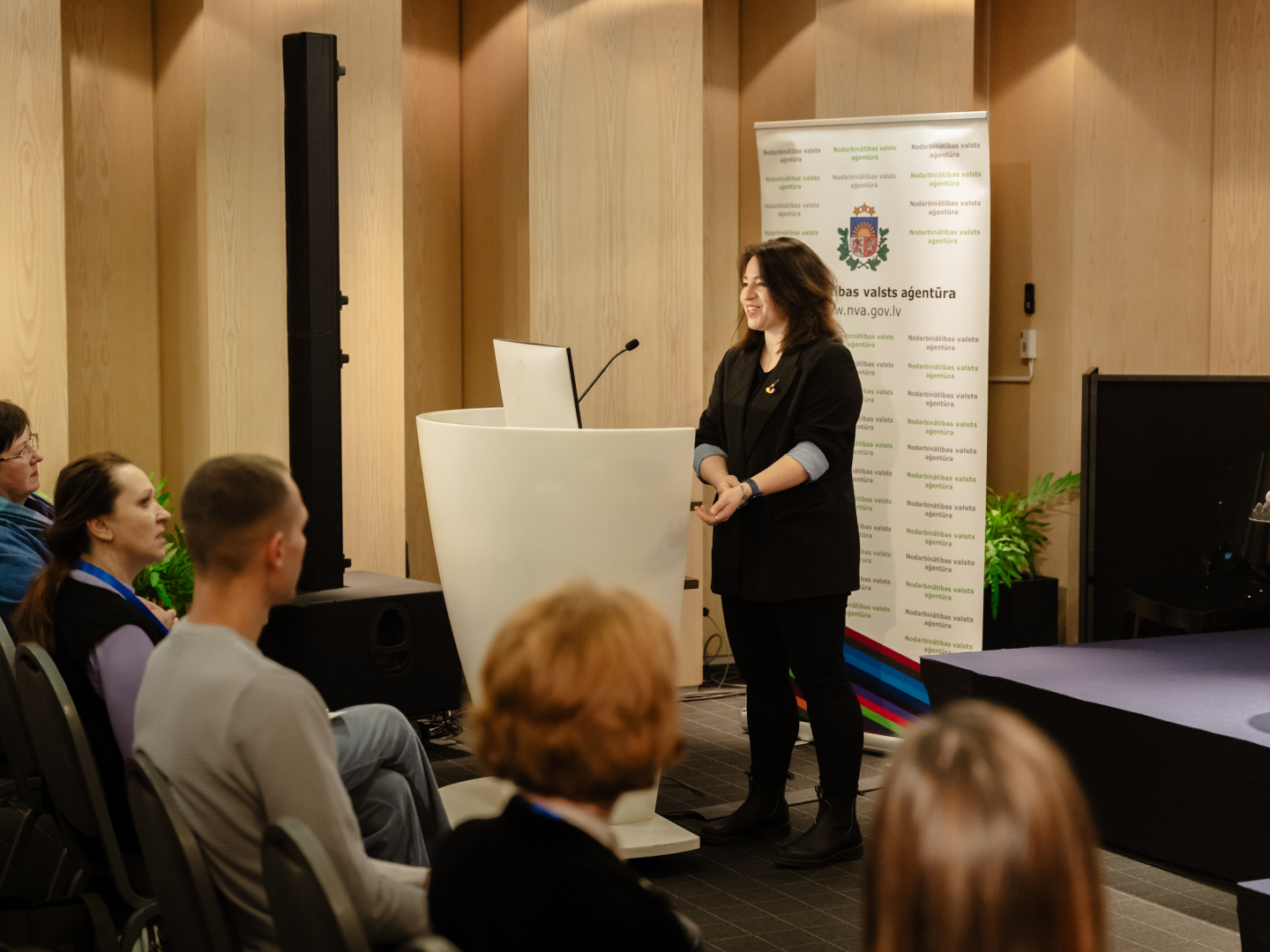 Konferences “Brīvprātīgais darbs Latvijā — vakar, šodien un rīt” foto ar plašu auditoriju, skatuvi un runātāju.